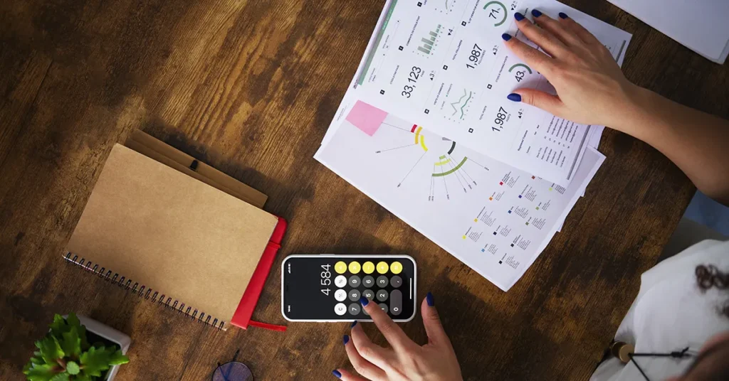 financial documents on a table next to a mobile calculator with a womans hands on both
