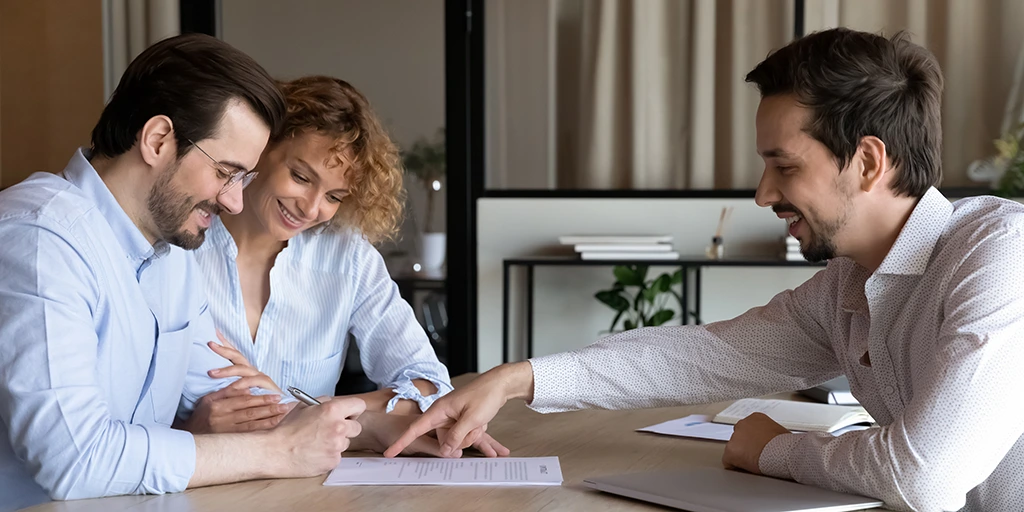 a couple sitting at a table with a loan officer signing for a loan